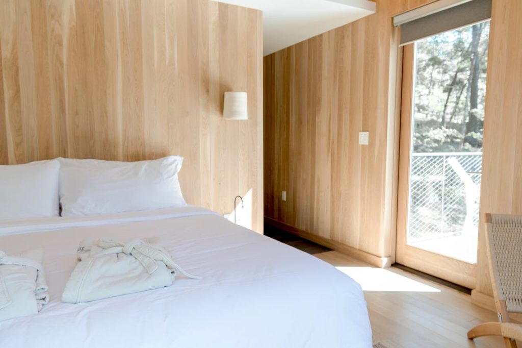 a-wooden-themed-bedroom-with-folded-white-robes-on-bed-9582421 Bright minimalist bedroom with large windows, wooden walls, and a cozy bed, offering a peaceful retreat.